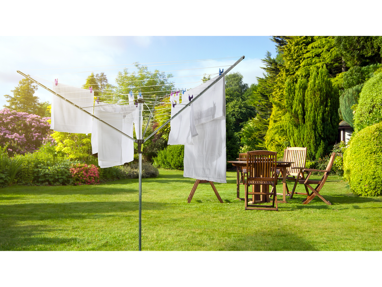 A rotary clothesline in a lush garden with white laundry drying in the sun.