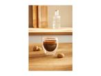 Espresso in a double-walled glass with two small cookies on a wooden counter.