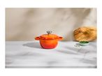 Orange cast iron pot with lid on a marble counter, next to a wooden board and chives.
