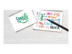 Two notebooks with handwritten phrases and a pen on a wooden surface.