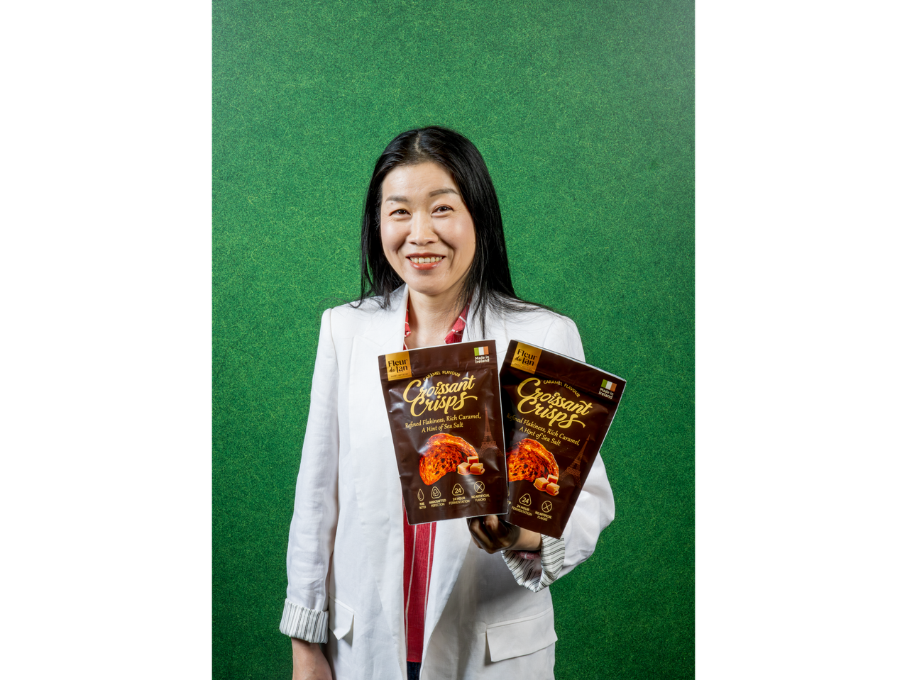 A woman holding two bags of Fleur de Lan Croissant Crisps against a green background.