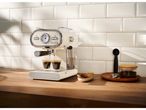 Cream-colored espresso machine brewing coffee into two glasses on a wooden counter.