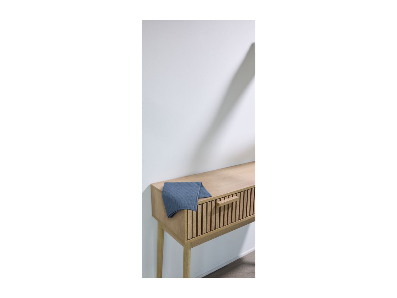 Wooden console table with a blue waffle-knit towel on top, against a white wall.