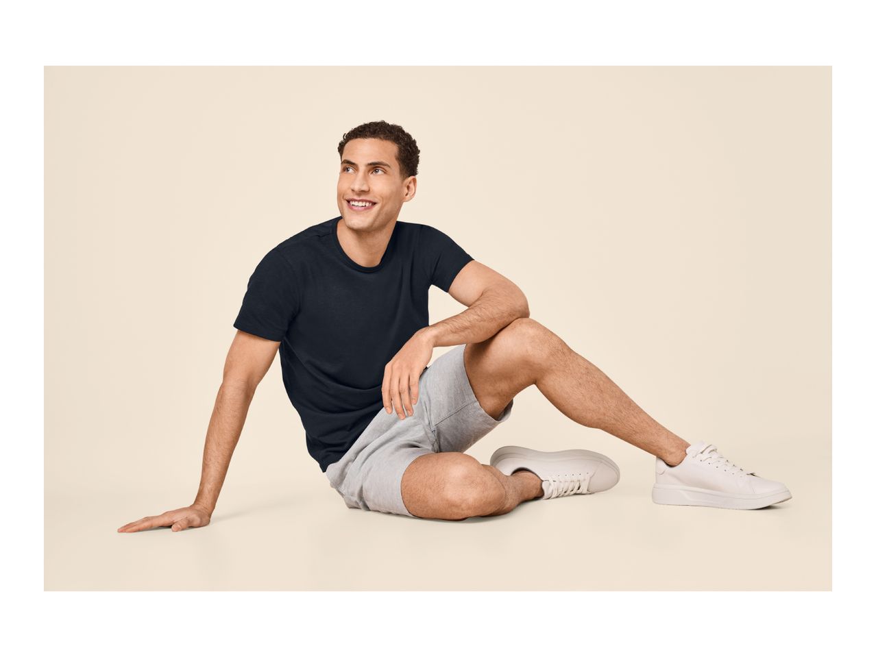 Man in a black t-shirt and grey shorts sitting on the floor, smiling and looking up.