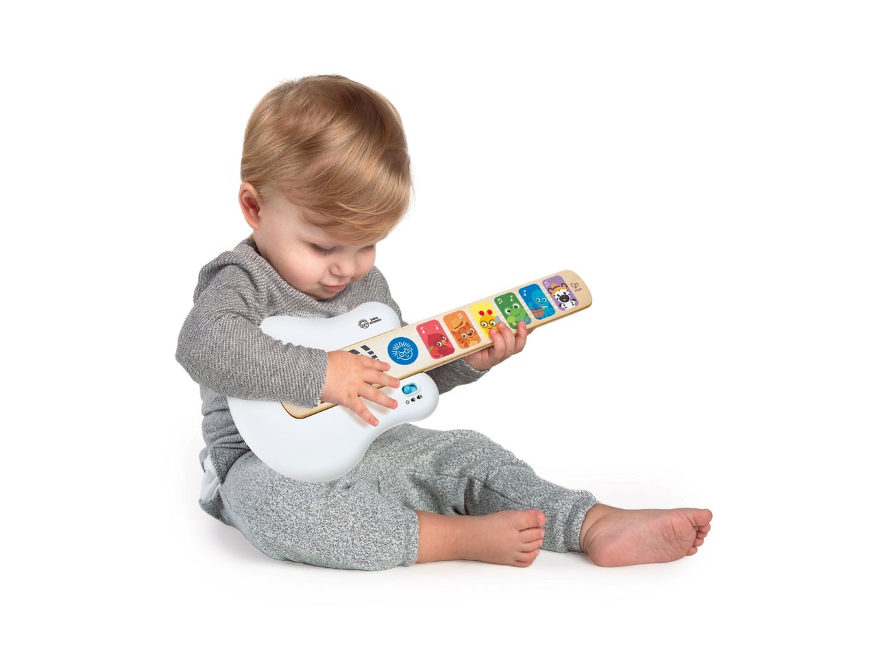 Toddler playing with a white and wooden toy guitar with colorful animal characters.