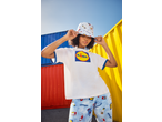 Woman in a white t-shirt with a large logo, bucket hat, and patterned shorts with groceries.