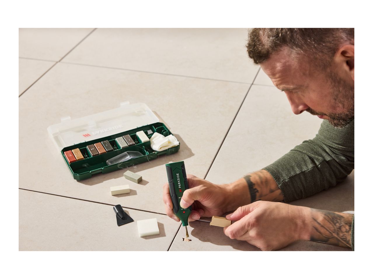 Man repairing floor tiles with a tile repair kit, melting filler into a grout line.