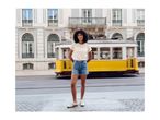 Woman in cream t-shirt and denim shorts, smiling in front of a yellow tram.