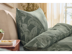Conjunto de roupa de cama verde com padrão de folhas num quarto luminoso.