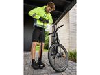 Man in a high-visibility jacket and cycling shorts pumping up a bicycle tire.