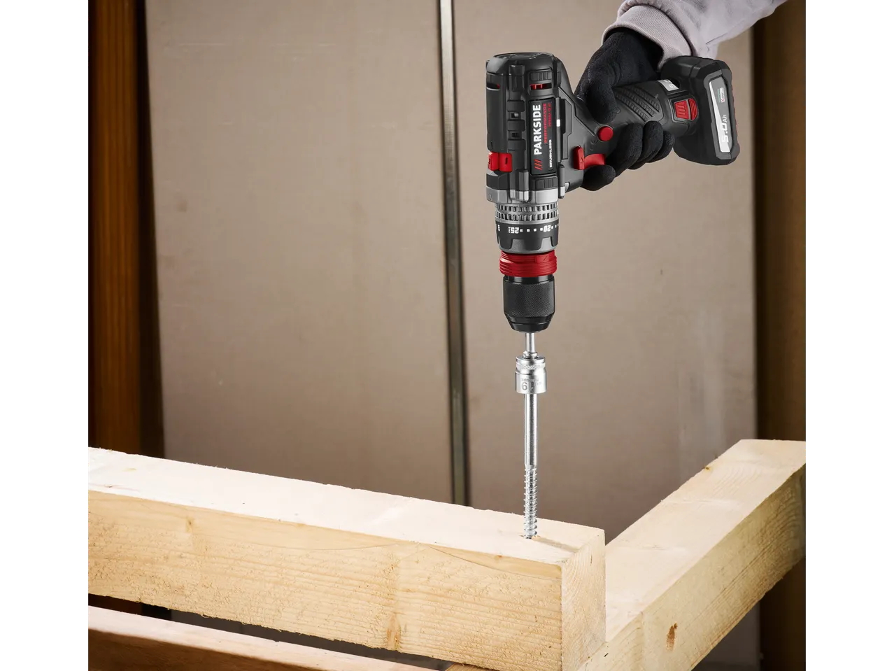 Una persona usa un trapano a batteria Parkside per avvitare in una trave di legno.