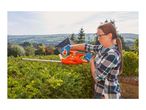 Woman trimming a hedge with an electric hedge trimmer in a garden with a scenic view.