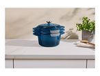 Three stacked blue cast iron pots with lids on a white countertop next to a potted plant.