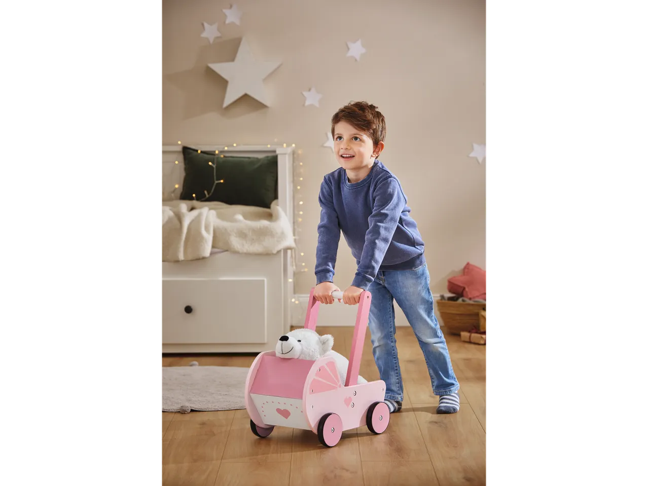 Menino empurrando um carrinho de bonecas Playtive com um ursinho de pelúcia.