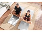 Două persoane meditează pe saltele de yoga gri.