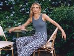 Woman in blue tank top and patterned trousers sitting at a table with a coffee cup.