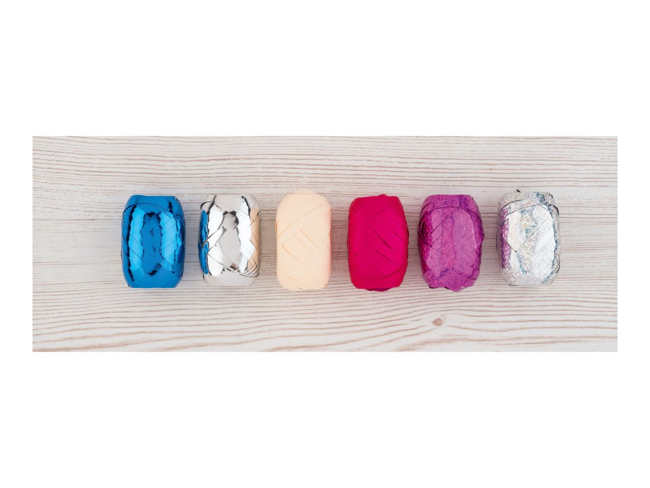 Six rolls of colorful curling ribbon on a light wooden surface.