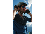 Man in cycling helmet, sunglasses, and gloves, adjusting helmet with mountains in background.