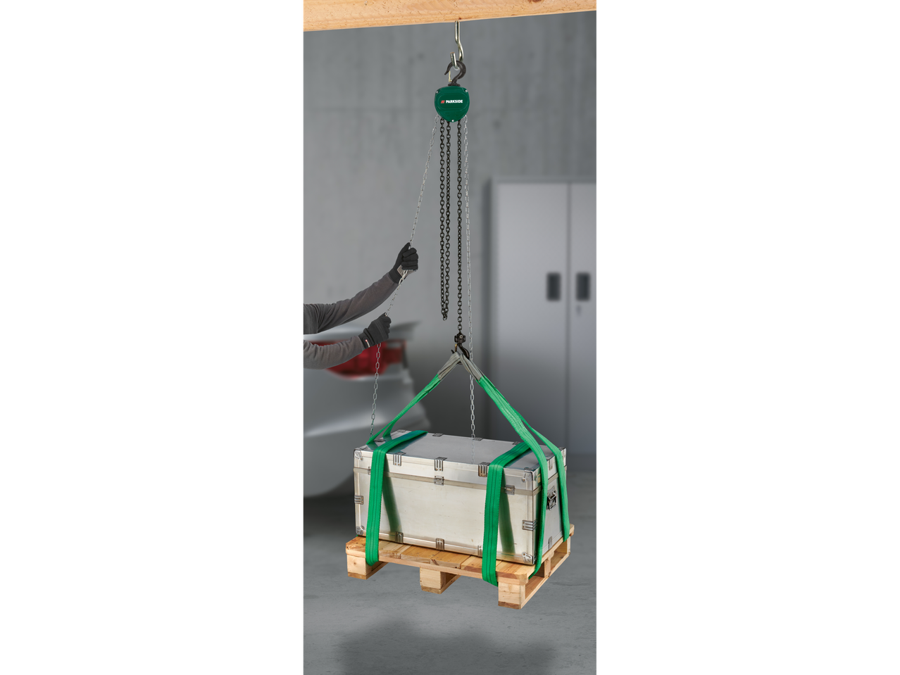 Person using a Parkside chain hoist to lift a metal box on a wooden pallet.