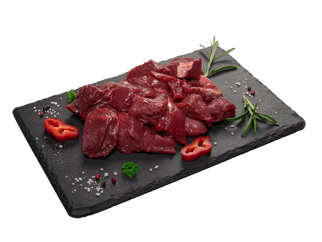 Nyers vadhús darabok, rozmaring, paprika és fűszerek egy fekete palatáblán.