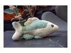 A soft, plush fish toy rests on a dark table, near a vase of flowers.