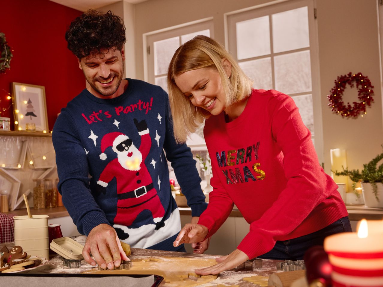 Couple in Christmas jumpers baking cookies with cookie cutters and baking ingredients.