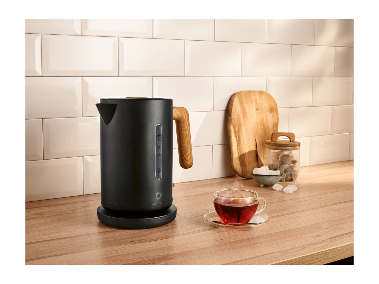 Black kettle with wooden handle on a kitchen counter with a cup of tea.