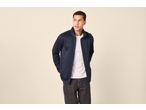 Man in marineblauwe jas en wit T-shirt, donkere broek, kijkt opzij.