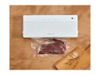 White vacuum sealer packaging a raw steak on a wooden surface next to a cutting board
