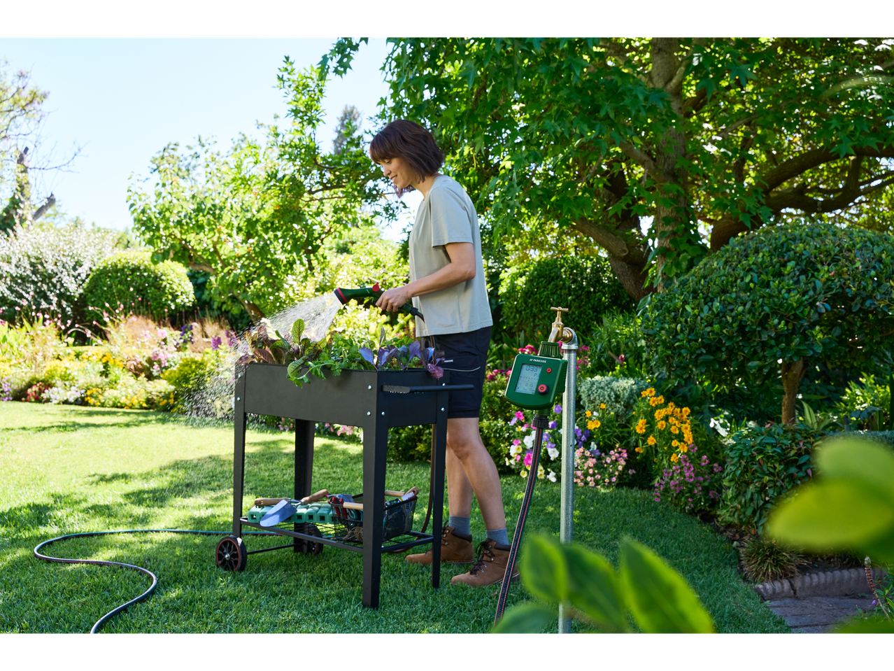 Žena zaliva biljke u podignutoj baštenskoj gredici sa Parkside multifunkcionalnim pištoljem za prskanje.