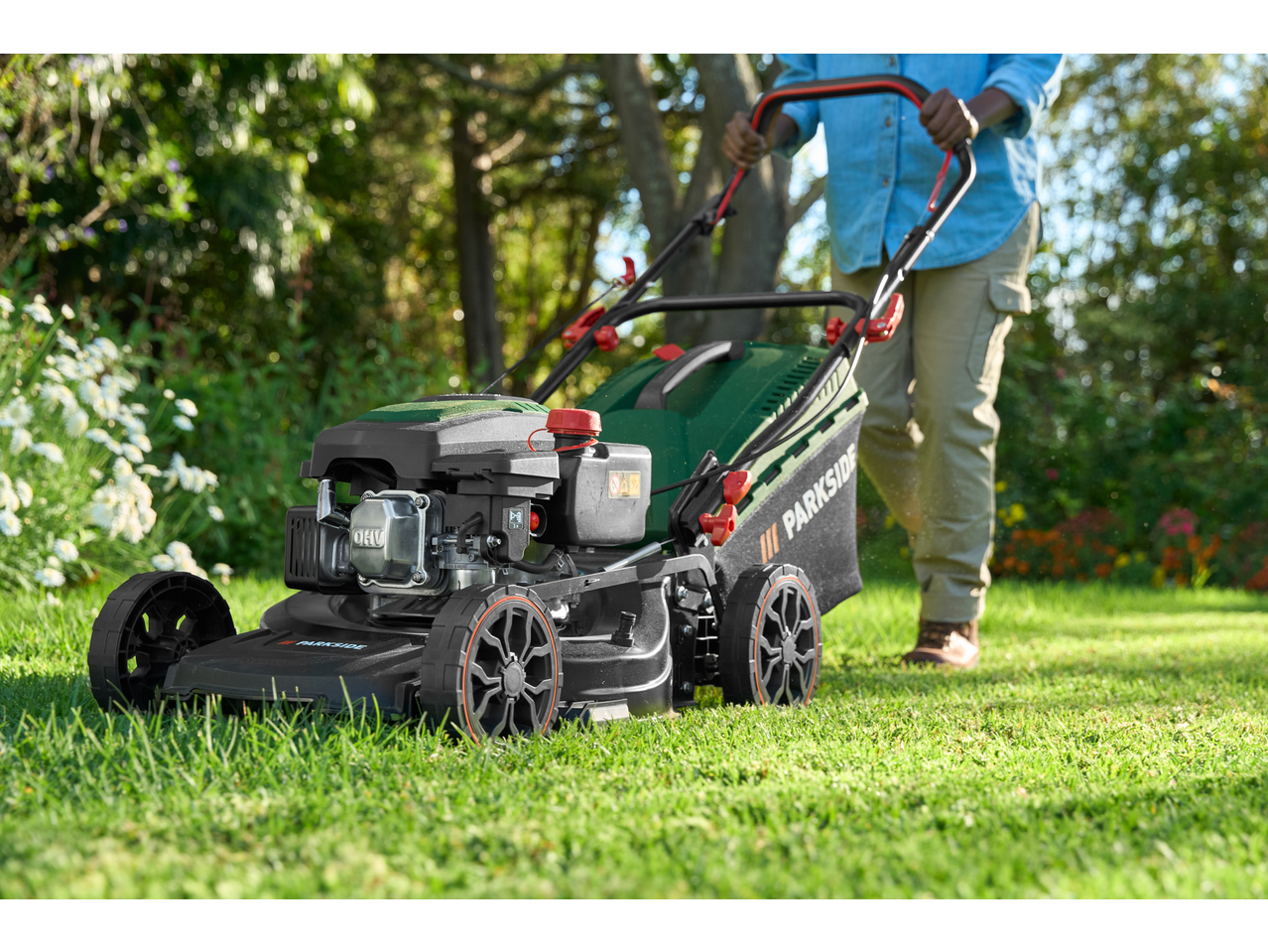 Parkside® Petrol Lawnmower being pushed across a green lawn by a person.