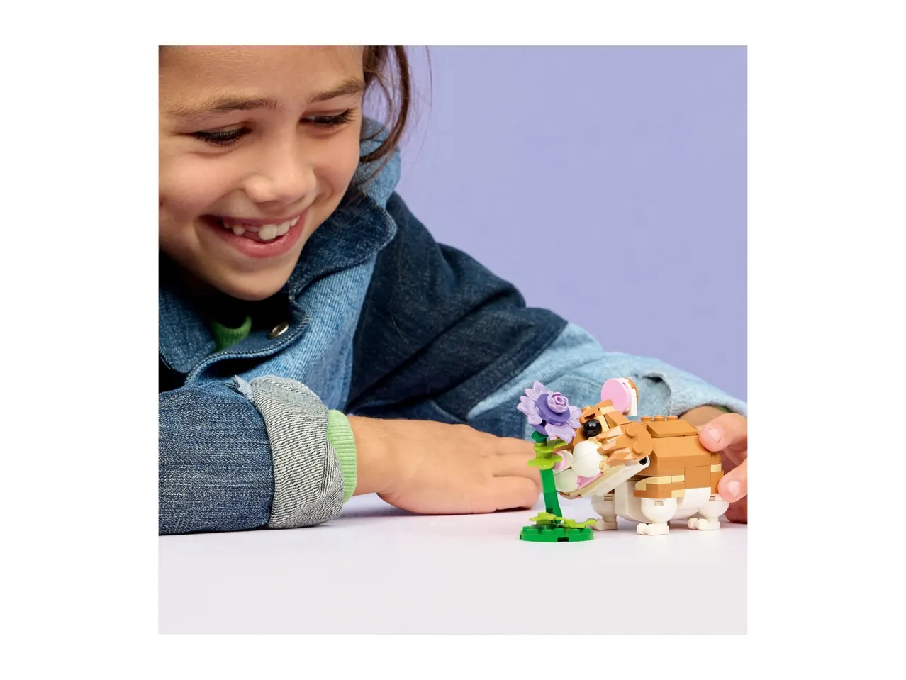 A smiling child playing with a toy hamster and a purple flower.