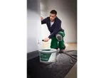 Ein Mann kniet, streicht mit einer Parkside Farbrolle eine Wand und hat einen Eimer Parkside Innen-Raumweiß Farbe daneben.
