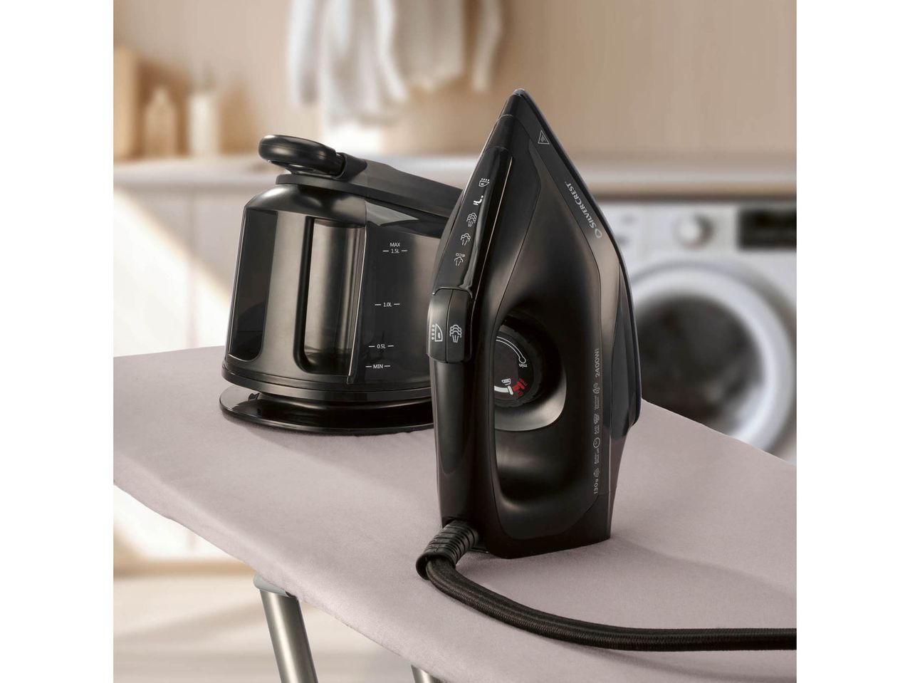 A black steam iron and its water tank on an ironing board in a laundry room.