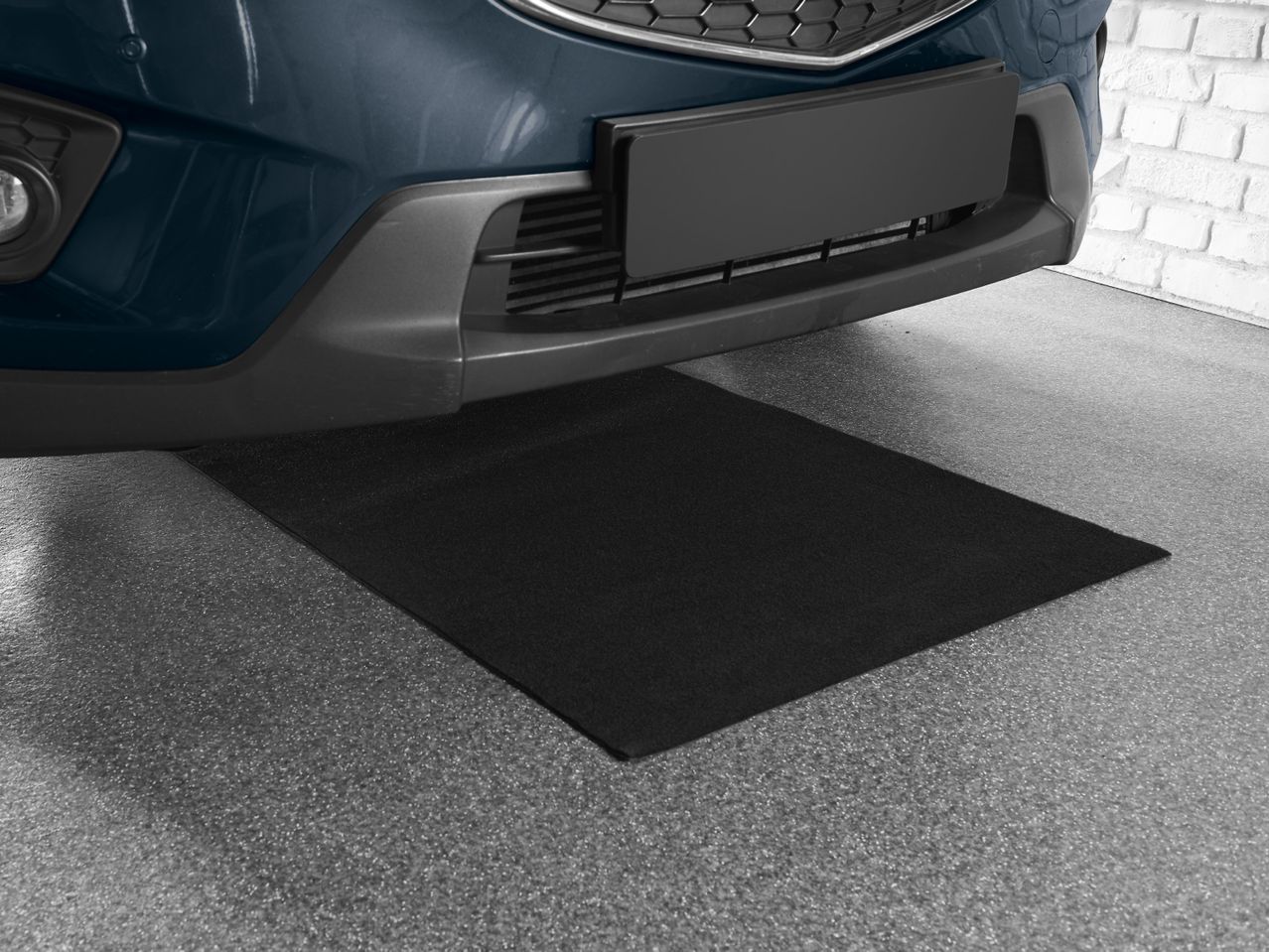 Dark blue car parked over a black garage floor mat on a gray speckled floor