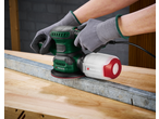 Hands in gloves operating a green and black PARKSIDE orbital sander on a wooden surface.