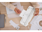 Laminador TRONIC sobre a mesa, mãos a colocar um documento para laminar.