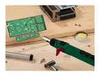 A soldering torch, circuit board, and soldering supplies on a wooden workbench.