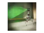 A green laser level on a tripod projects lines onto a wall in a room under construction.