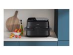 Black air fryer on a kitchen counter with tomatoes and olive oil.