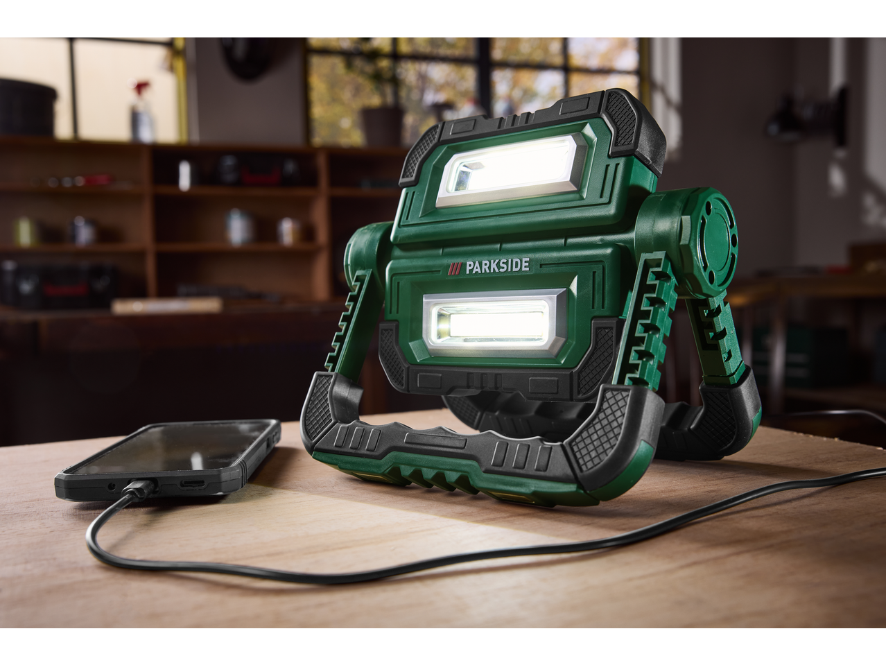 Proiector LED PARKSIDE încărcând un telefon pe o masă de lemn.