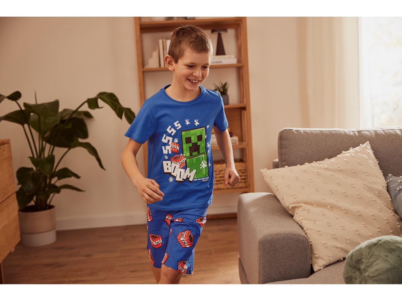 Boy wearing Minecraft pajamas runs playfully in a living room.