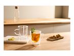 Two double-walled glass mugs, one with tea and garnishes, on a wooden kitchen counter.