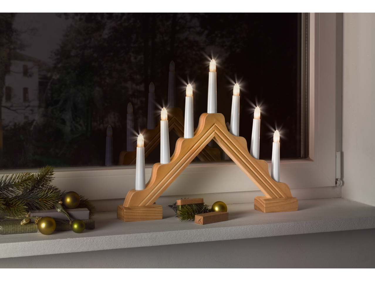 Apšviestas medinis žvakių lankas ant palangės su kalėdinėmis dekoracijomis naktį