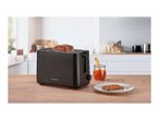 Black toaster with a slice of toast, jam, and a plate on a wooden kitchen counter.