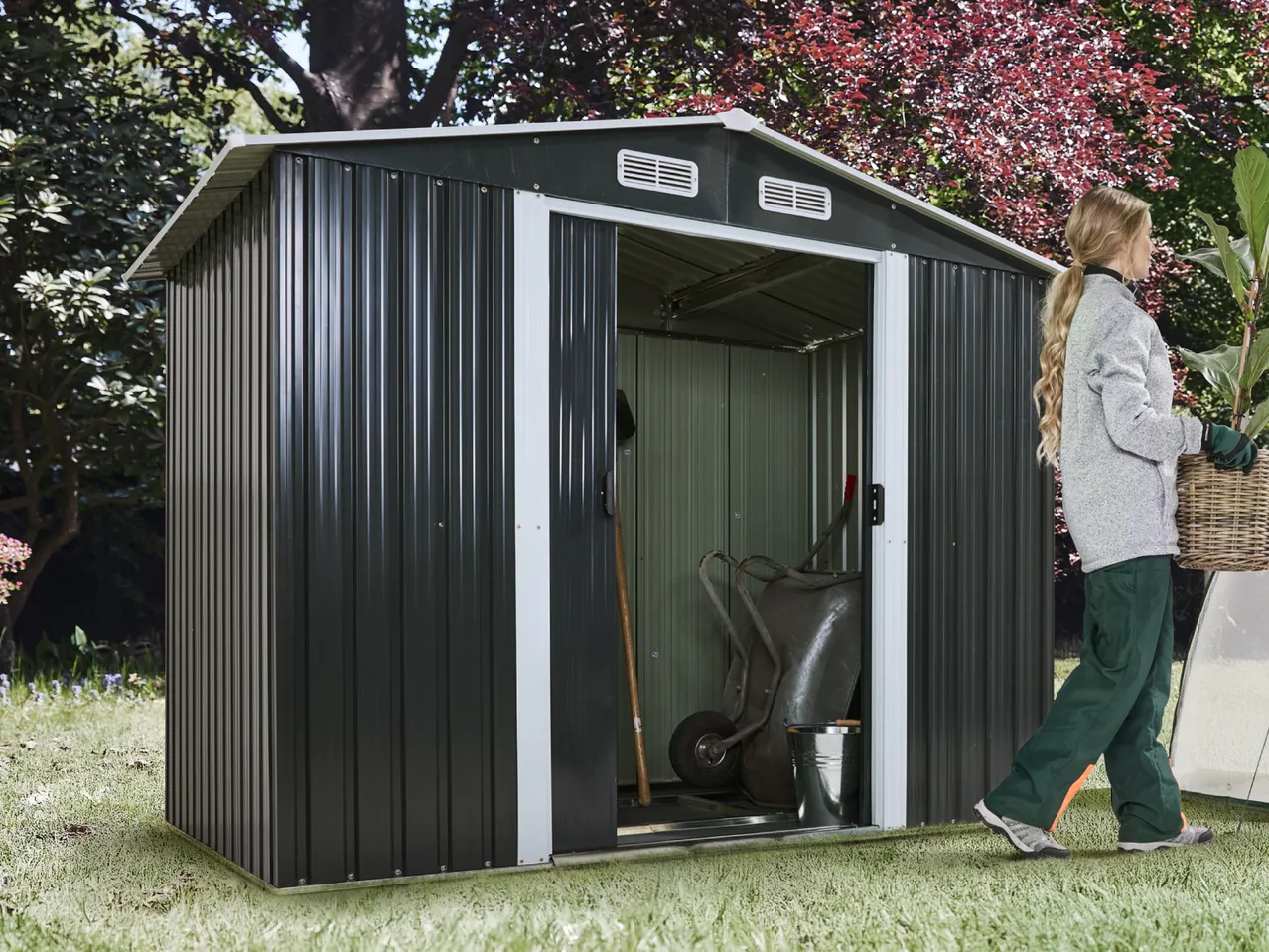 Dark grey garden shed with open door, garden tools inside, and a person carrying a plant.
