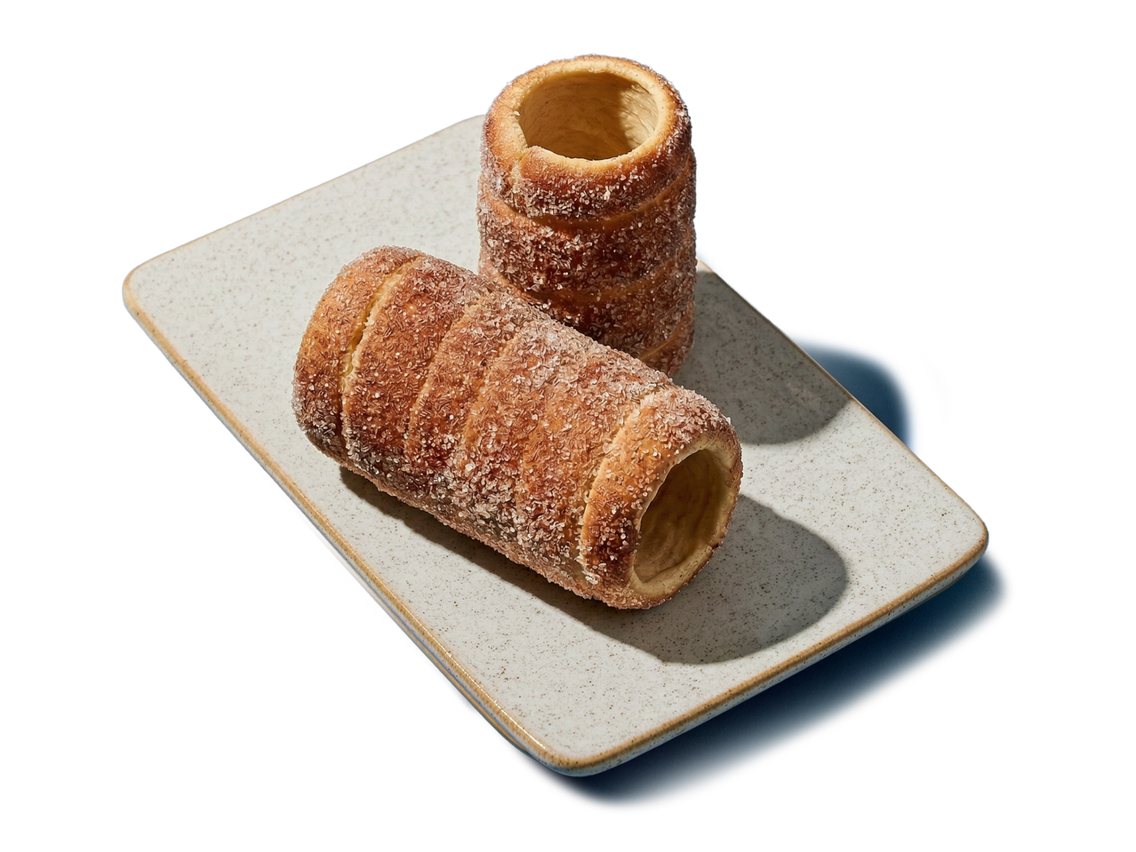 Două cozonaci kurtos kalacs cu zahăr, așezați pe o farfurie dreptunghiulară.