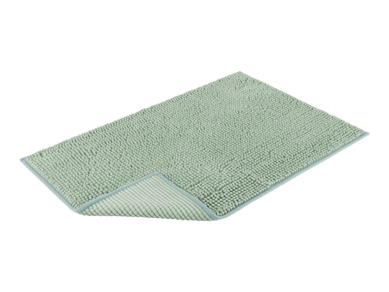 A sage green bath mat with a textured surface is shown at a slight angle.