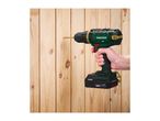 A cordless drill with a gold drill bit is held by a hand, drilling into a wooden surface.