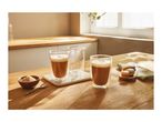 Two double-walled glasses, one with a latte, on a wooden table with sugar and macarons.